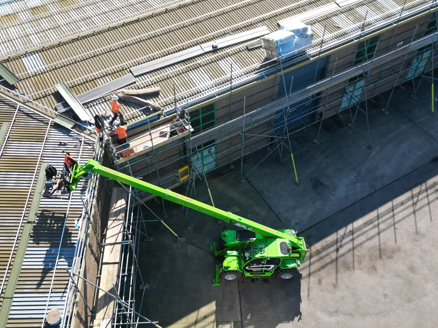 Telehandler lifting new roof sheets onto the building
